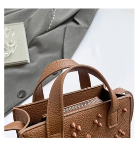 Gros plan sur la texture du cuir marron à motif litchi et rivets métalliques du sac