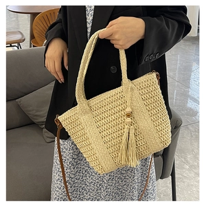 Detail van geweven rieten handtas met boho-kwastjes en bruine leren schouderband voor