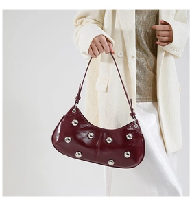Détail du sac en cuir verni bordeaux avec clous argentés porté par un mannequin en blazer