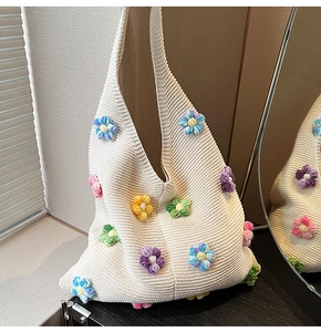 Détail d'un sac hobo en tricot crème avec des fleurs 3D colorées au crochet et texture