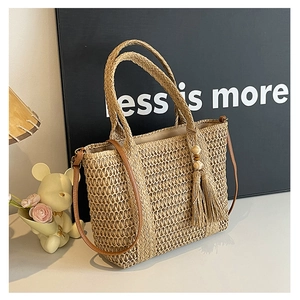 Detail of hand-woven straw beach bag with leather straps and decorative tassel hanging