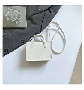 Détail du sac à bandoulière blanc à motif litchi placé à côté d'un costume gris foncé