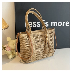 Detail view of woven straw tote bag featuring leather straps and decorative beaded tassels