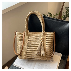 Close-up of handmade straw tote bag with brown leather strap and tassel detail