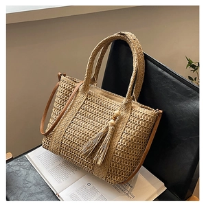 Detail of woven straw handbag featuring leather straps and decorative wooden bead tassels