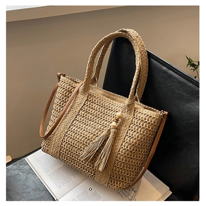 Detail of straw tote bag showing natural weaving, brown leather straps, and fringe tassels