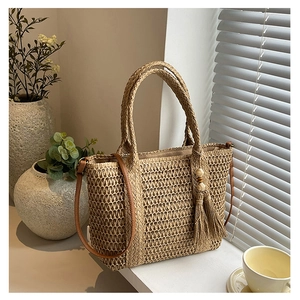 Straw tote bag detail with fine weave, wooden bead tassel, and adjustable leather strap