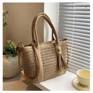 Close-up of woven straw bag with leather strap and decorative tassel with wooden beads