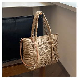Close-up of woven straw tote bag featuring leather straps and ethnic tassel charm details
