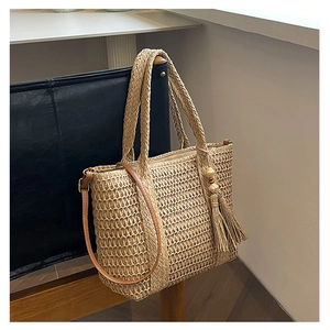 Detail of woven straw tote bag with brown leather straps and decorative wooden beads