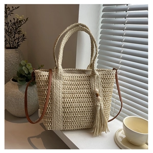 Detail of straw woven tote bag featuring a wooden bead tassel and brown leather shoulder strap