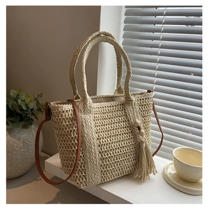 Detail of woven straw tote bag with brown leather strap and wooden bead tassel decor