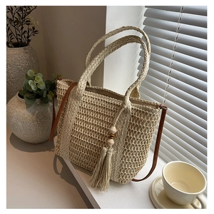 Detail of straw woven tote bag featuring decorative tassel charms and long shoulder straps