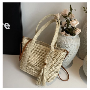 Detail of woven straw beach bag with tassel charms and slim brown leather strap