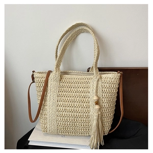 Close-up of beige woven beach bag featuring brown leather straps and beaded tassel detail