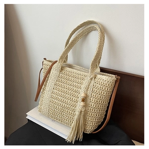 Close-up of woven straw tote bag featuring detailed fringe and slim leather shoulder strap