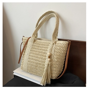 Detail of straw tote bag featuring wood bead tassels and brown leather shoulder straps