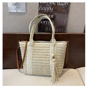 Close-up of woven straw tote bag featuring wood bead tassel and leather shoulder strap