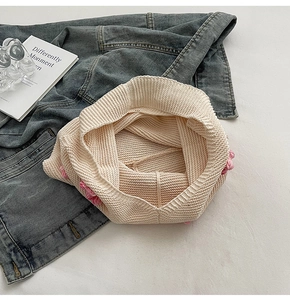 Détail d'un bonnet en maille beige avec trois fleurs roses faites à la main en laine