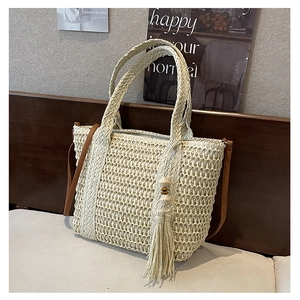 Detail of straw woven bag featuring mesh hollow design, fringe tassel and leather strap