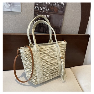 Detail of straw woven tote bag featuring beige texture, tassels and brown leather strap