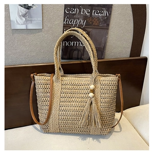 Detail of woven straw tote bag with brown leather handles and tassel on a sofa