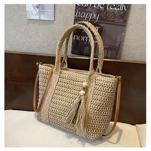 Detail of woven straw handbag featuring boho tassels, wooden beads, and a slim shoulder strap