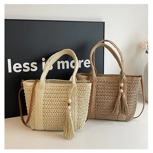 Detail view of woven straw handbags in cream and light brown with tassel and wood beads