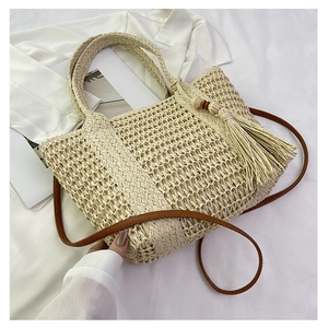 Detail of hand-woven beige straw bag featuring a wooden bead tassel and crossbody strap