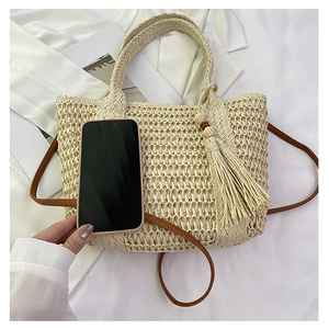 Detail of hand-woven straw bag showing textured fiber and brown leather strap with smartphone