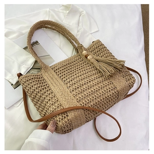 Close-up of woven straw bag with leather handles, shoulder strap and tassel charm