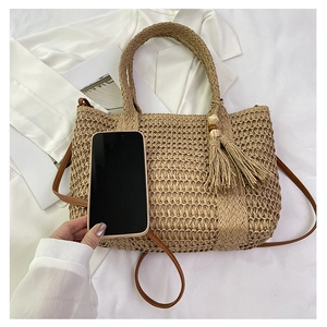 Detail of straw tote bag showing raffia weave texture, tassel charms and wood beads