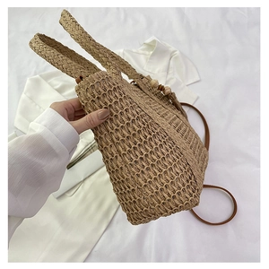 Close-up of light brown woven straw tote bag with leather strap on white linen background