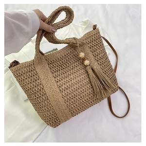 Detail of woven straw tote bag with brown leather strap and tassel wood bead charm