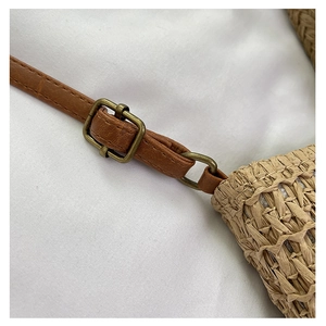 Detail of adjustable brown leather strap and bronze metal buckle on a woven straw bag