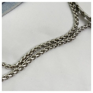 Close-up of a twisted silver metal chain strap for fashion handbags on a fabric background
