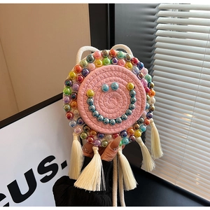Detail of pink woven round bag featuring beaded smile face and white silk fringes