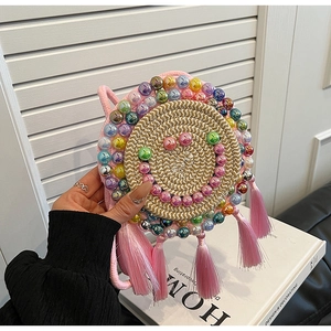 Detail of hand-woven round straw bag with colorful bead smiley face and pink tassels