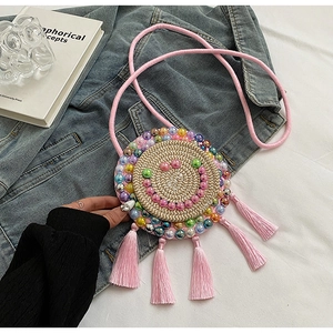 Detail of woven straw circle bag featuring a colorful beaded smiley face and pink tassels