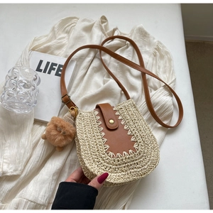 Détail du sac en paille tressée avec bandoulière en cuir brun et pompon décoratif