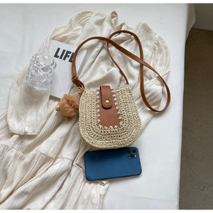 Détail d'un sac besace en paille tressée avec bandoulière cuir et charme peluche