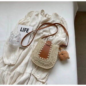 Détail du sac bandoulière en paille avec garniture en cuir et charme sur robe