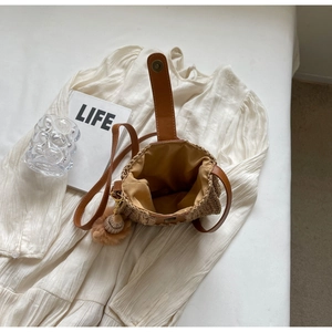 Détail du sac seau en paille avec bandoulière en cuir et pompon sur une robe d'été