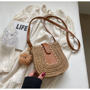 Détail d'un sac en paille tressée avec bordure en cuir et pompon brun sur chemise blanche
