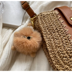 Détail d'un sac en paille tressée avec pendentif en peluche et bandoulière en cuir