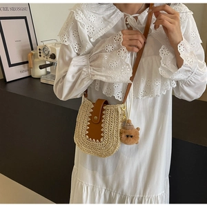 Detail of straw crossbody bag with brown leather flap and cute bear charm accessory