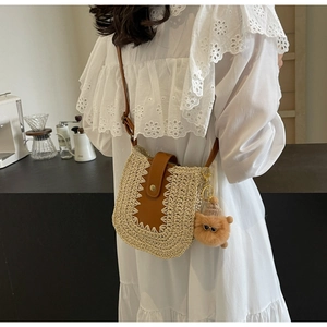 Détail d'un sac bandoulière en paille avec rabat en cuir marron et breloque peluche
