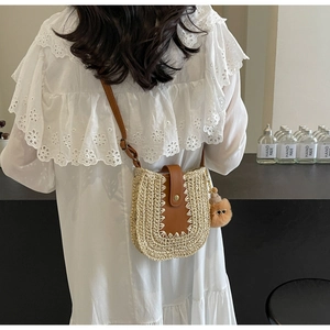 Détail d'un petit sac bandoulière en paille tressée avec rabat en cuir sur robe blanche