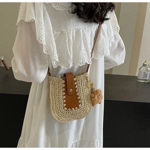 Détail du sac en paille tissée avec bandoulière en cuir brun et pompon décoratif