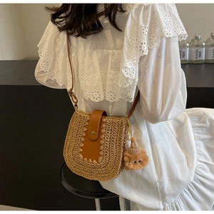 Détail d'un sac en paille tissé avec rabat en cuir marron et breloque ours en peluche